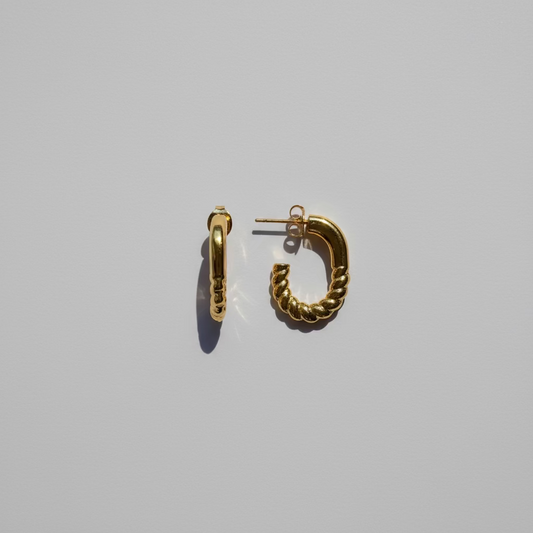 Gold hoop earrings on a thin rod against a light background